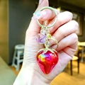 Porte-clés fraise tenu en main avec ferrures dorées et détail de perle violette - Fraise Électroplaquée Rouge Or