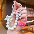 Gros plan d'un porte-clés perlé fait main avec flacon cœur et petit nœud blanc décoratif - Coeur aux Haricots Laiteux / Rouge