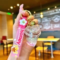 Detailed close-up of pink heart-shaped liquid quicksand keychain with gold bell and honey strap - White