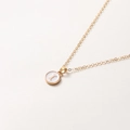 Détail d'une chaîne dorée avec pendentif rond en émail blanc orné de la lettre L dorée - Lettre I