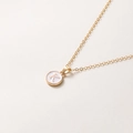 Détail du collier chaîne dorée avec pendentif rond blanc orné de la lettre K gravée - Lettre K