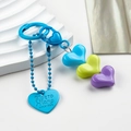Dettaglio di ciondoli a cuore in resina colorata e targhetta in metallo blu incisa - Cuore Blu Verde Viola