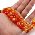 Primer plano de cuentas de ágata natural a rayas rojas y naranjas en la mano - Naranja