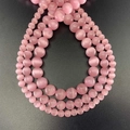 Detailed view of round pink cat's eye stone beads in various sizes on a black background - Pink
