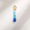 Close-up of a gradient blue enamel capsule charm with gold plating and hook detail - Letter I