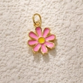 Macro shot of gold-plated daisy pendant with pink enamel petals on white sand surface - Pink Daisy Shape (A0811)