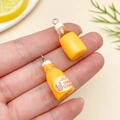 Close-up of a mini orange milk bottle charm with organic label held in hand - Transparent Yellow (24079)