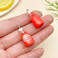 Close-up of miniature resin milk bottle pendants with organic labels and metal hooks - Transparent Red (24078)