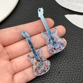 Detail of acrylic guitar pendants with blue floral prints and glitter, held in hand - Transparent Blue Guitar (24051)