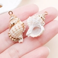 Ciondolo in conchiglia naturale con bordi galvanizzati in oro tenuto nel palmo - Stile Di Conchiglia Bianca Lattea Con Textura Naturale (25315) / 1 Pezzo/Confezione (24x15mm) / Oro