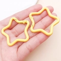 Detail of hand holding two bright yellow star-shaped metal keychains with spring gate hooks - Yellow (FT188)