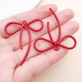 Dettaglio di ciondoli a fiocco rosso con trama scanalata tenuti in mano per scala - 42x37mm / Rosso