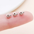 Macro view of small copper crimp beads for jewelry making held on a fingertip for scale - Flat White K (19158)