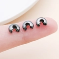 Macro shot of gun-black C-shape fold-over jewelry crimp beads held on fingertip - Large Gun Black (25601)