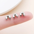 Macro detail of silver Crimp Covers for jewelry making held on a fingertip - Large White K (25598)