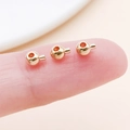 Three tiny polished gold crimp beads for DIY jewelry held on a fingertip for size - Round KC Gold (26048)