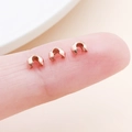 Three rose gold C-shaped crimp bead covers for jewelry making held on a fingertip - Small Rose Gold (25583)