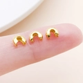 Three small gold-plated Crimp Bead Covers for DIY jewelry making displayed on a fingertip - Medium Gold (25592)
