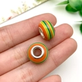 Primer plano de cuentas de resina con rayas verdes y naranjas sostenidas para ver escala - Estilo Rayado Naranja-Verde (11545)