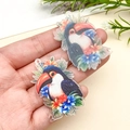 Détail macro de deux breloques toucan en acrylique pour la création de bijoux DIY - Perroquet Bleu avec Fleur (23947)