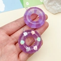 Dettaglio di ciondoli a forma di ciambella in resina viola con glitter e cartoni - Viola Trasparente