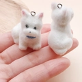 Close-up of white flocked puppy pendants held in hand for DIY jewelry and crafts - Sitting Dog with Blue Scarf (24805) / 33x30x19mm