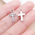 Vue macro de deux pendentifs en forme de croix argentée pour bijoux DIY tenus dans la main - Croix Creuse en Alliage de Zinc Argent Antique (22329)