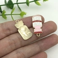 Dettaglio di un ciondolo a scudo dorato e charm in smalto rosa per la creazione di gioielli DIY - Flacone di medicina rosa