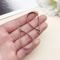 Primer plano de dos colgantes de gota en bronce para bisutería DIY en la mano - Marco de Gota de Agua (22380)