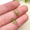 Macro detail of tiny translucent green acrylic leaf charms held on a fingertip for DIY jewelry - Light Dark Green Mini Leaf (22135)