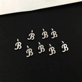 Close-up of eight silver cursive letter B alloy pendants with top rings for jewelry making - Letter B