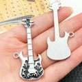Detail van gitaarhangers in de hand, met zwarte druppelolie en gestreept metalen design - Zwart Emaille Hip Hop Gitaar (22347)