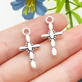 Pendentif croix argenté texturé pour bijoux DIY, présenté sur le doigt pour l'échelle - Croix Ovale en Alliage de Zinc Argent Antique 12x23mm (18726)