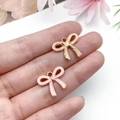 Macro detail of alloy pink enamel bow charms and gold textured pendants for DIY jewelry - Small Hollow Bowknot