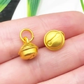 Matte gold bell charms for DIY jewelry making shown on fingertip for scale - Solid Antique Gold Silent Small Bell