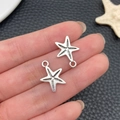 Détail de deux pendentifs étoile de mer argentés avec texture réaliste en main - Breloque Étoile de Mer (22909)
