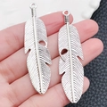 Ciondoli a piuma in lega d'argento vintage per gioielli fai-da-te, mostrati sulla mano - 15x62mm / Ciondolo Piuma Grande Argento Antico (7183)