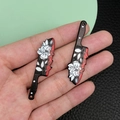 Detailed close-up of acrylic knife pendants with white rose pattern and red splatter - Black Acrylic Flower With Blood Prop (19276)