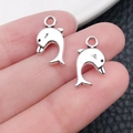 Handheld view of two antique silver dolphin pendants for DIY jewelry making - Marine Dolphin (11187)