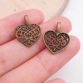 Close-up of vintage bronze heart-shaped hollow charms held to show scale and detail - Hollow Heart Charm (4193)