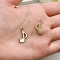 Detail van muzieknoot hangers in goud en wit op de handpalm voor de maatreferentie - Muzieknoot Stijl (19449) / 1 Stuk (19x12mm) / Wit