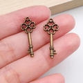 Macro detail of two vintage bronze clover-top key pendants held by hand for scale - Four Leaf Clover Heart Key (20990) / Antique Bronze