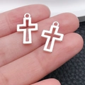 Detailed macro view of silver cross charms held by hand for DIY jewelry making projects - Glossy Hollow Cross Style (20363)