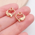 Golden heart wing charms for DIY jewelry making shown between fingertips for scale - Heart Wings (19980)