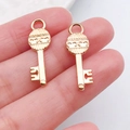 Detailweergave van twee goudkleurige sleutelhangers voor DIY-sieraden op een vingertop - Golfkop Sleutel (21006)