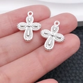 Pair of bright silver cross pendants with textured details held by hand to show small size - Radial Pattern Cross Style (20350)