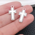 Pair of silver-plated cross pendants with beaded edges held on a finger for size view - Beaded Edge Cross Style (20356)