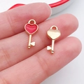 Macro detail of red enamel and gold heart key pendants held between fingers for size reference - Heart Key (17525)