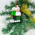 Dettaglio di un ciondolo natalizio in resina dipinto a mano appeso a un albero decorato - Stile Slitta Membri della Famiglia