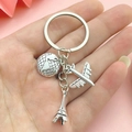 Silver Eiffel Tower, globe, and airplane travel keychain held against a pink background - Travel Universal Style (ER541)